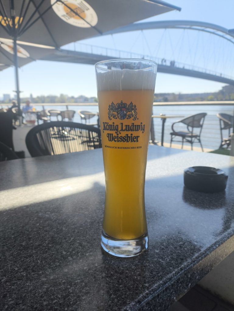 A glass of weissbier with the Rhine river and the three countries footbridge in the background