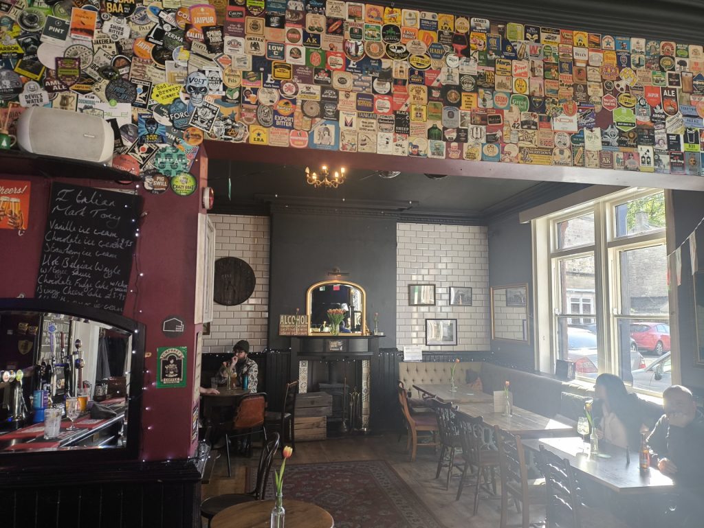 Interior of The Tannery pub on Gilesgate in Hexham showing a wall full of pump clips and drinkers at tables in the bar area