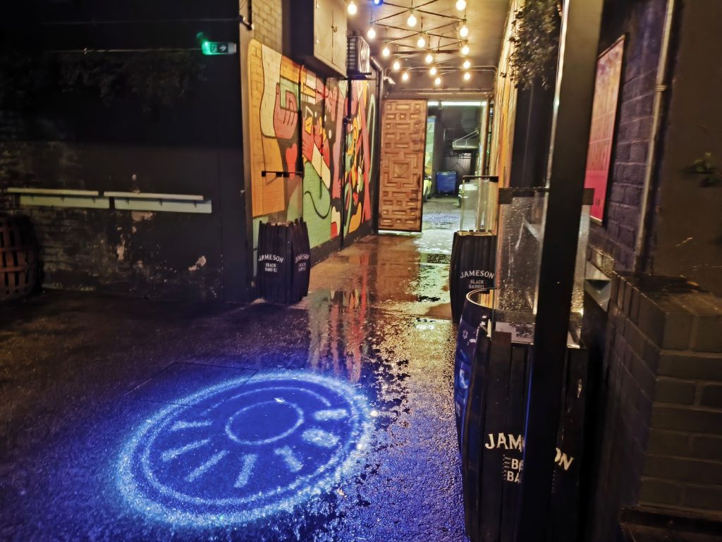 Entrance to the Bullitt Espresso Bar with rain soaked pavement and a projected "BULLITT" sign