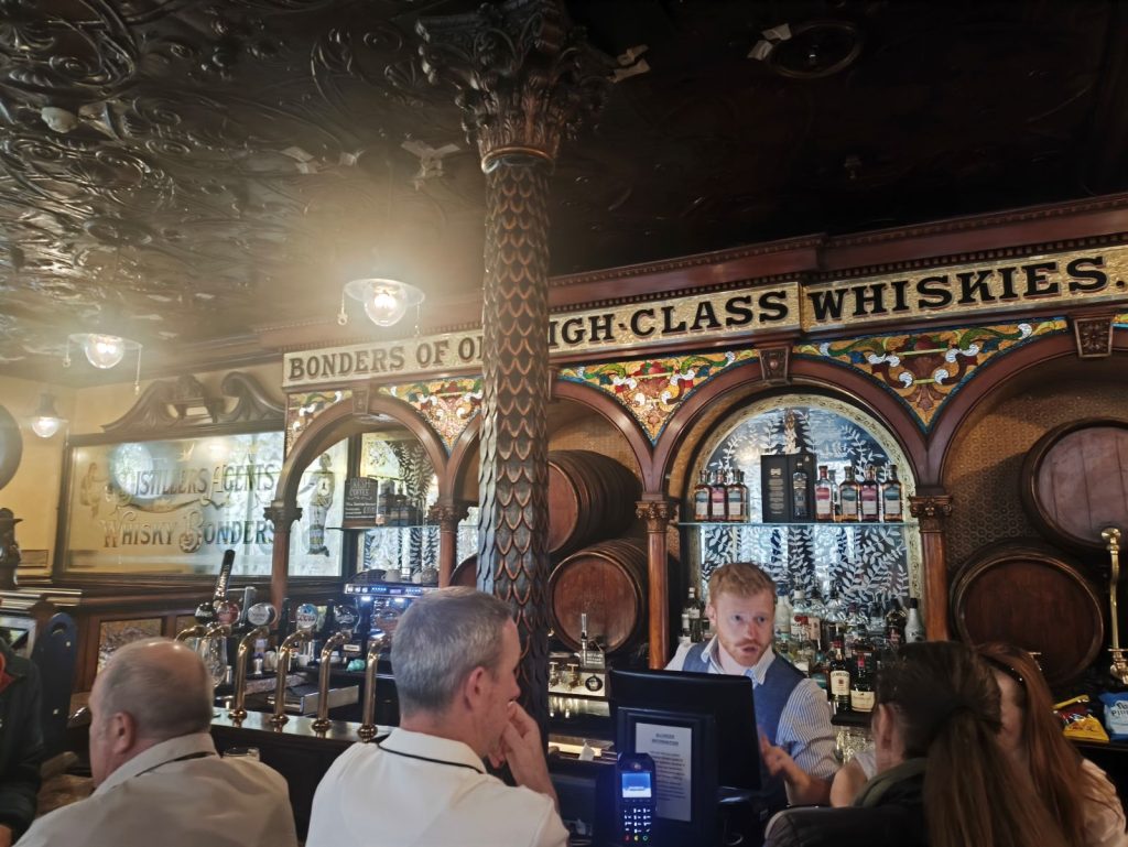 The bar back and customers in the Crown Liquor Saloon in Beflast showing tiled details and casks.