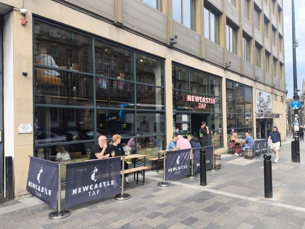 Exterior of the Newcastle Tap showing outside seating and groups of people socialising.